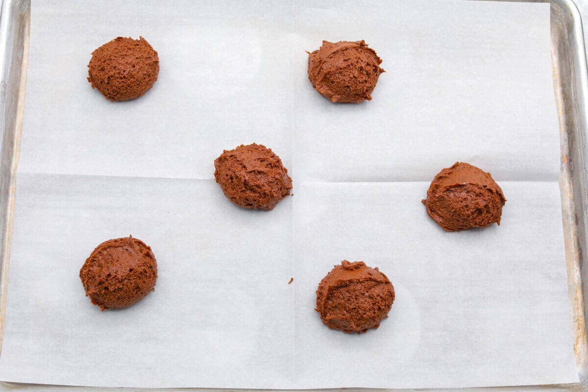 Balls of cookie dough added to a cookie sheet with parchment paper.