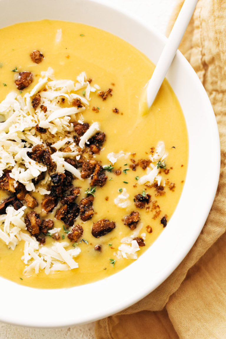 Pumpkin soup in a bowl with walnut crispies and cheese on top.