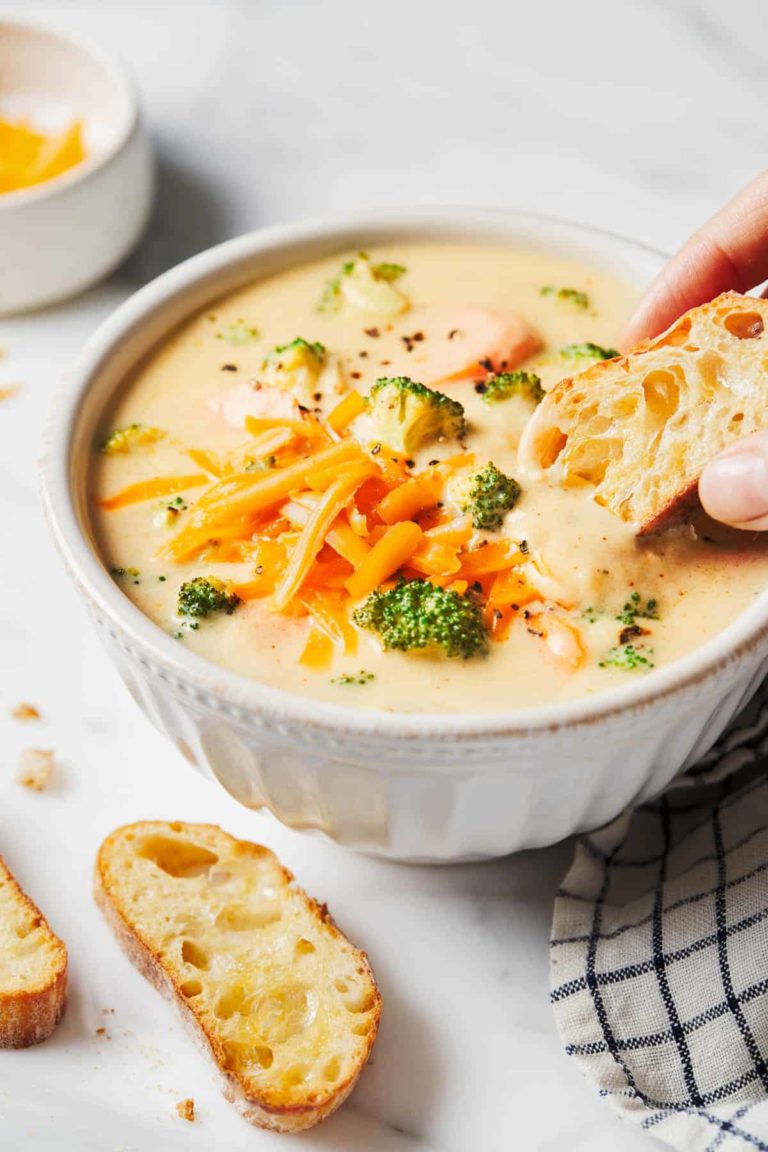 Broccoli cheese soup in a bowl with bread being dipped in.