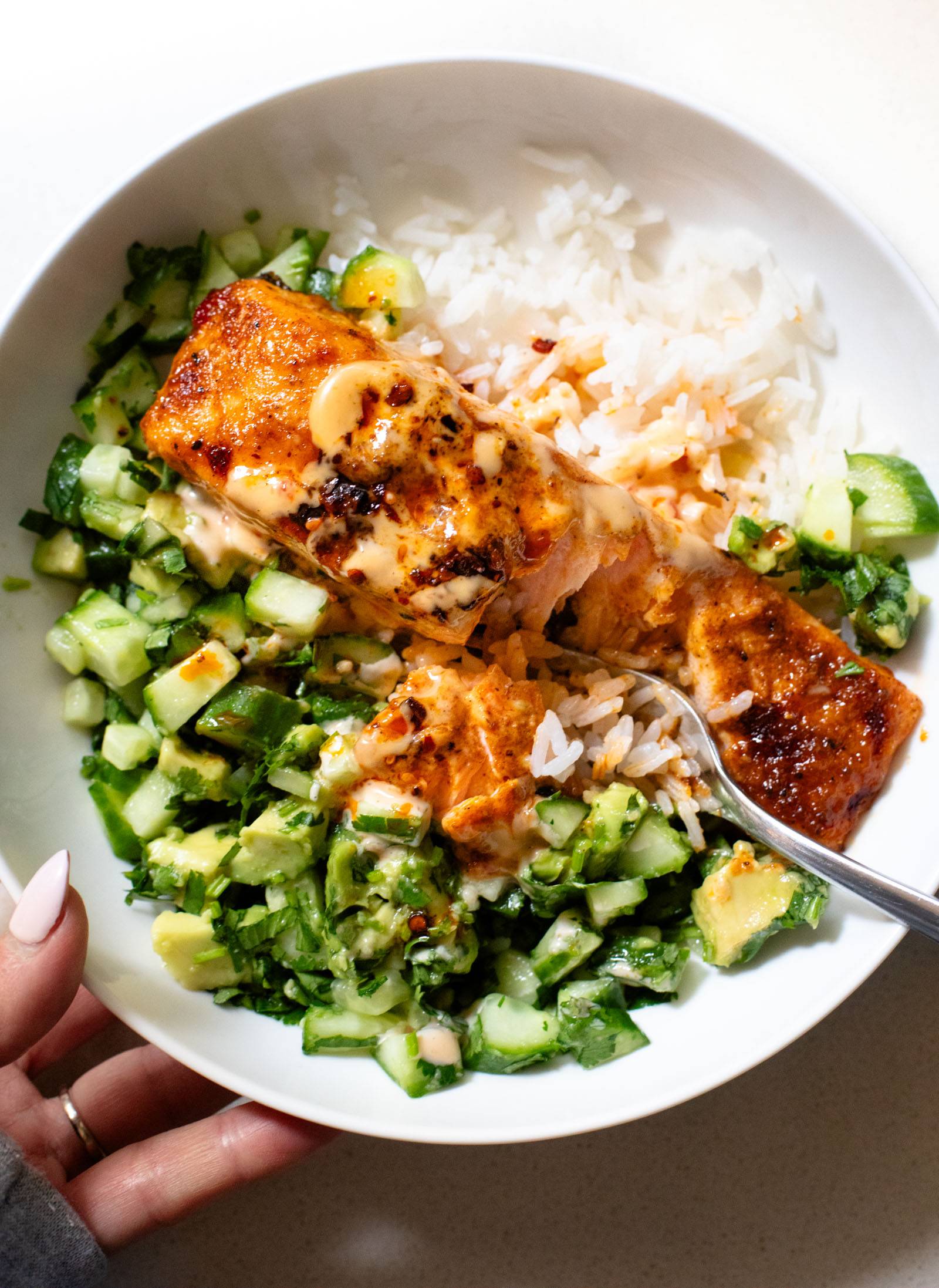 Bang bang salmon in a bowl with white rice and avocado cucumber salsa.