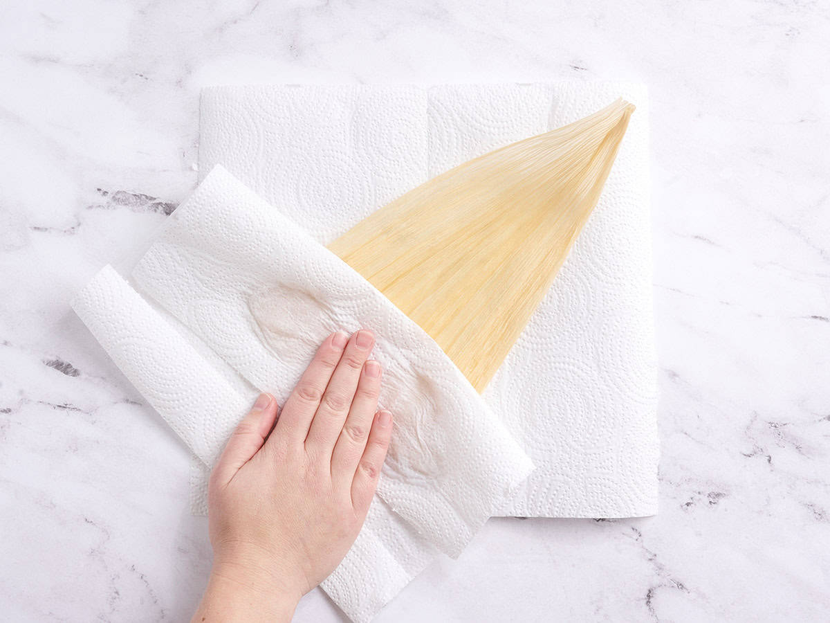 A hand using a paper towel to dry a corn husk.