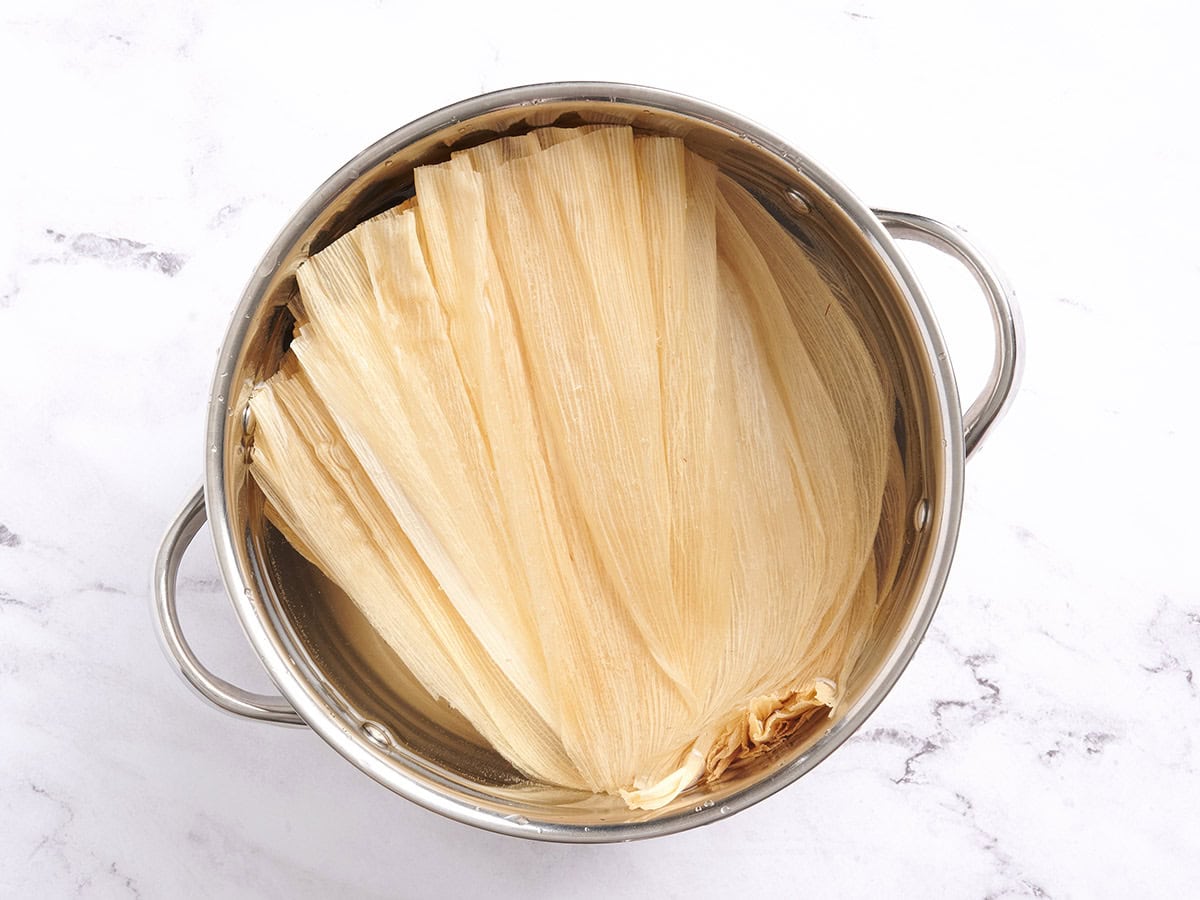 Corn husks soaking in a sauce pan of water.