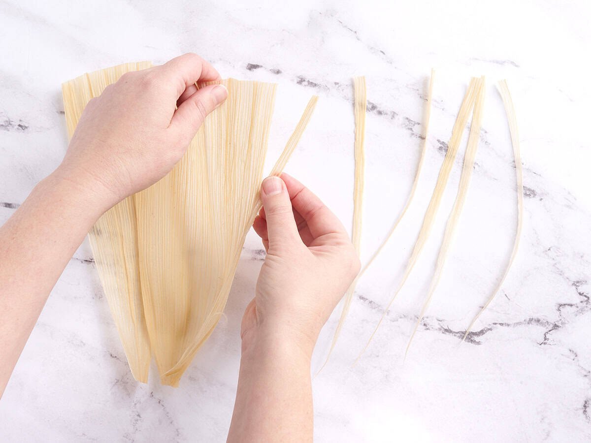 Hands shredding a corn husk.