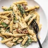 Close up of one pot creamy pesto chicken pasta in a shallow bowl with a black fork.