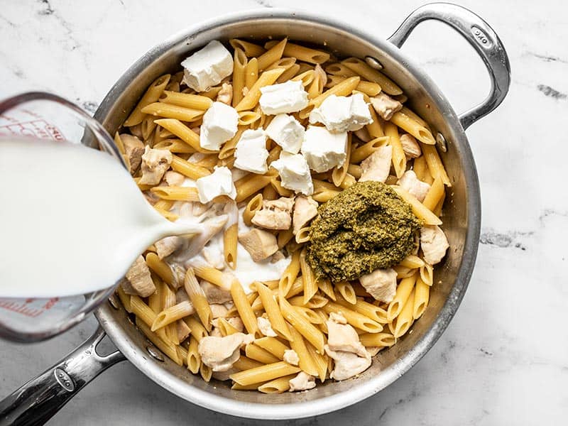 Milk being poured into the skillet with chunks of cream cheese and pesto.