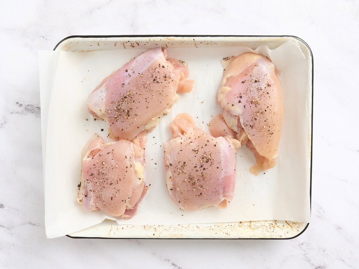 Seasoned chicken thighs on a baking sheet.