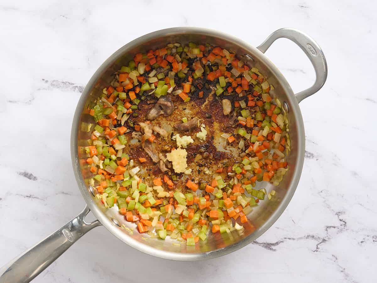 Garlic and seasonings added to sauteed mirepoix in a skillet.