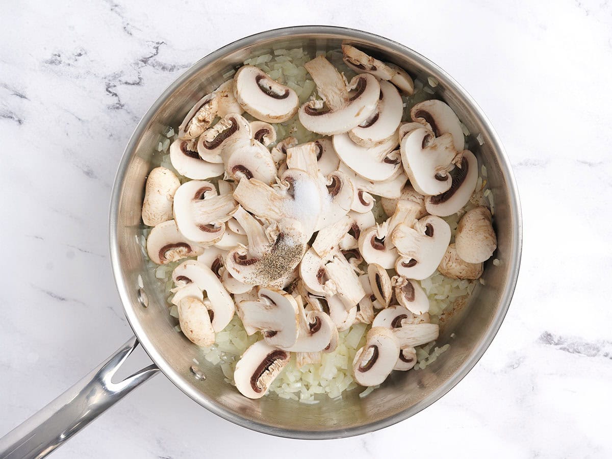 Mushrooms added to sauteed onions in a skillet.