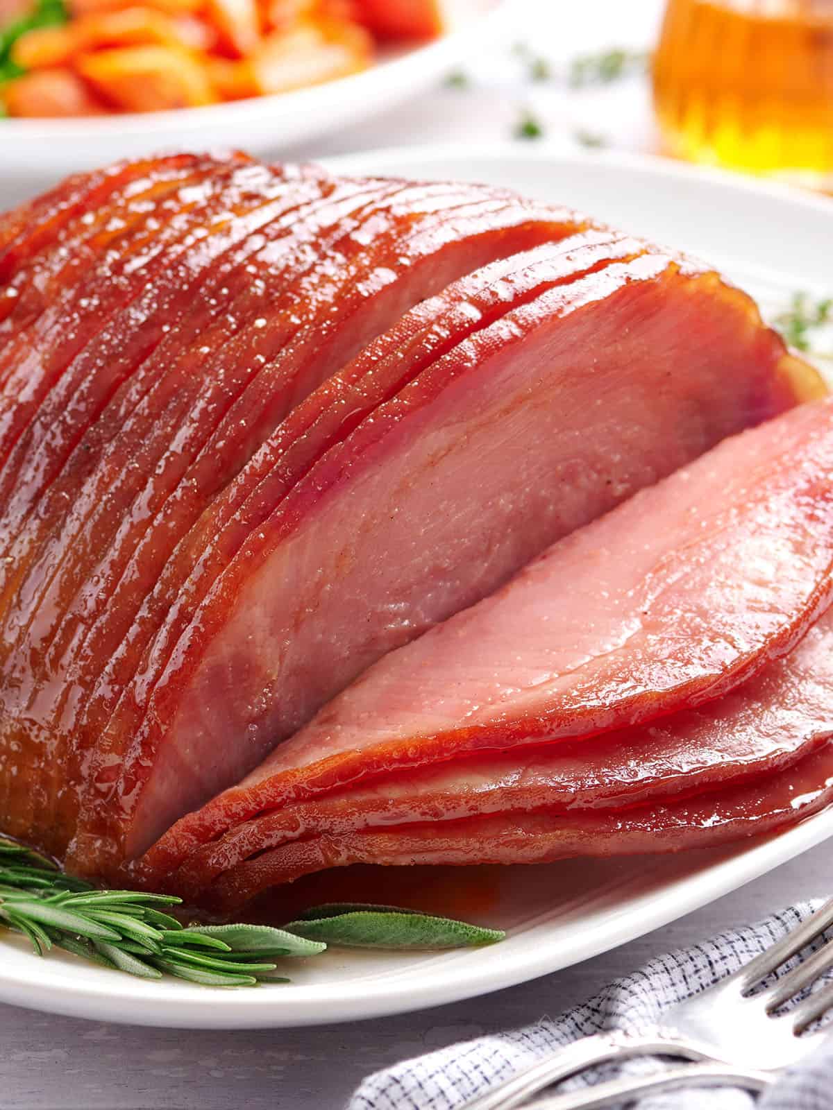Side view of sliced honey glazed ham on a plate with herbs.