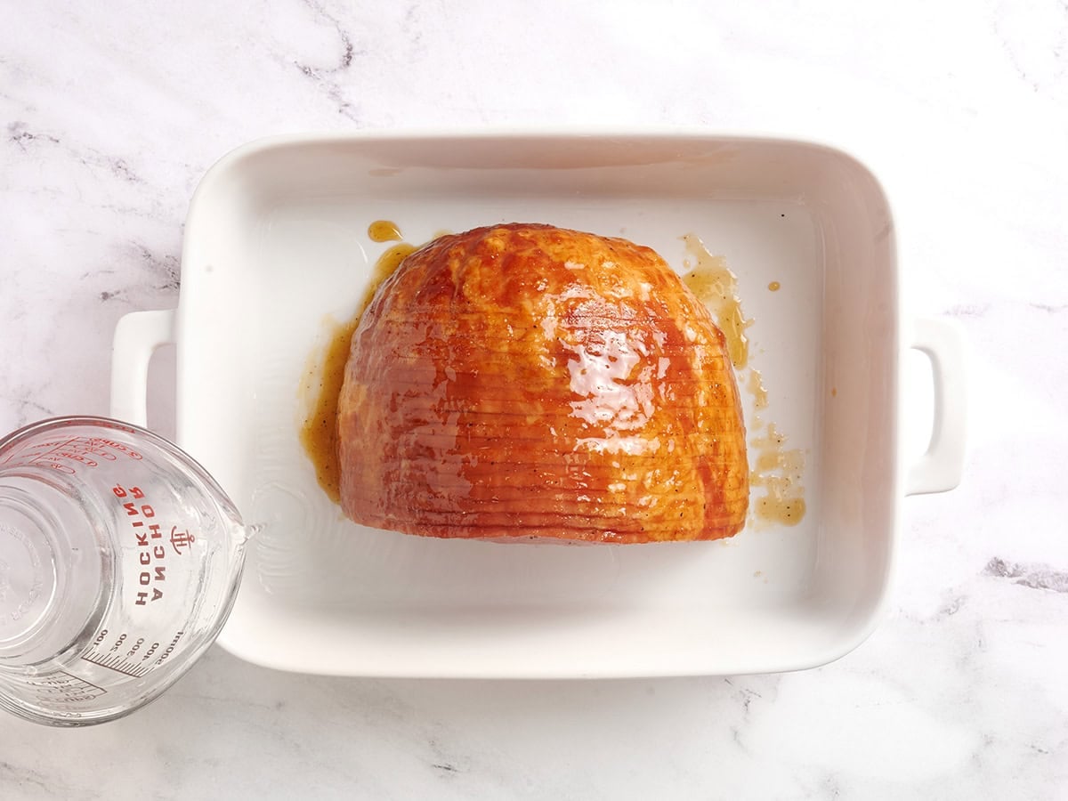 Water being poured into a baking dish with honey glazed ham.