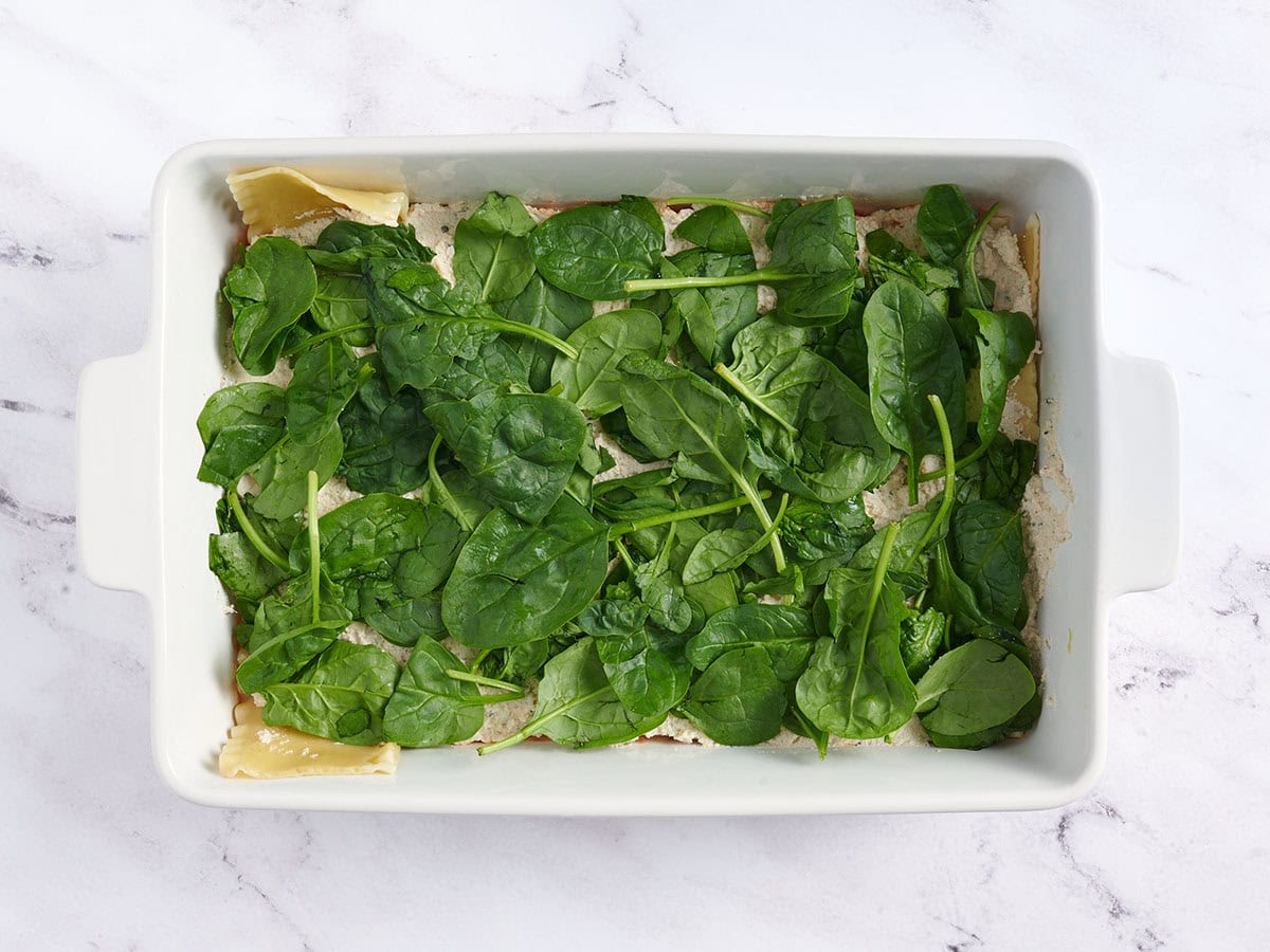 Spinach added to vegan lasagna.