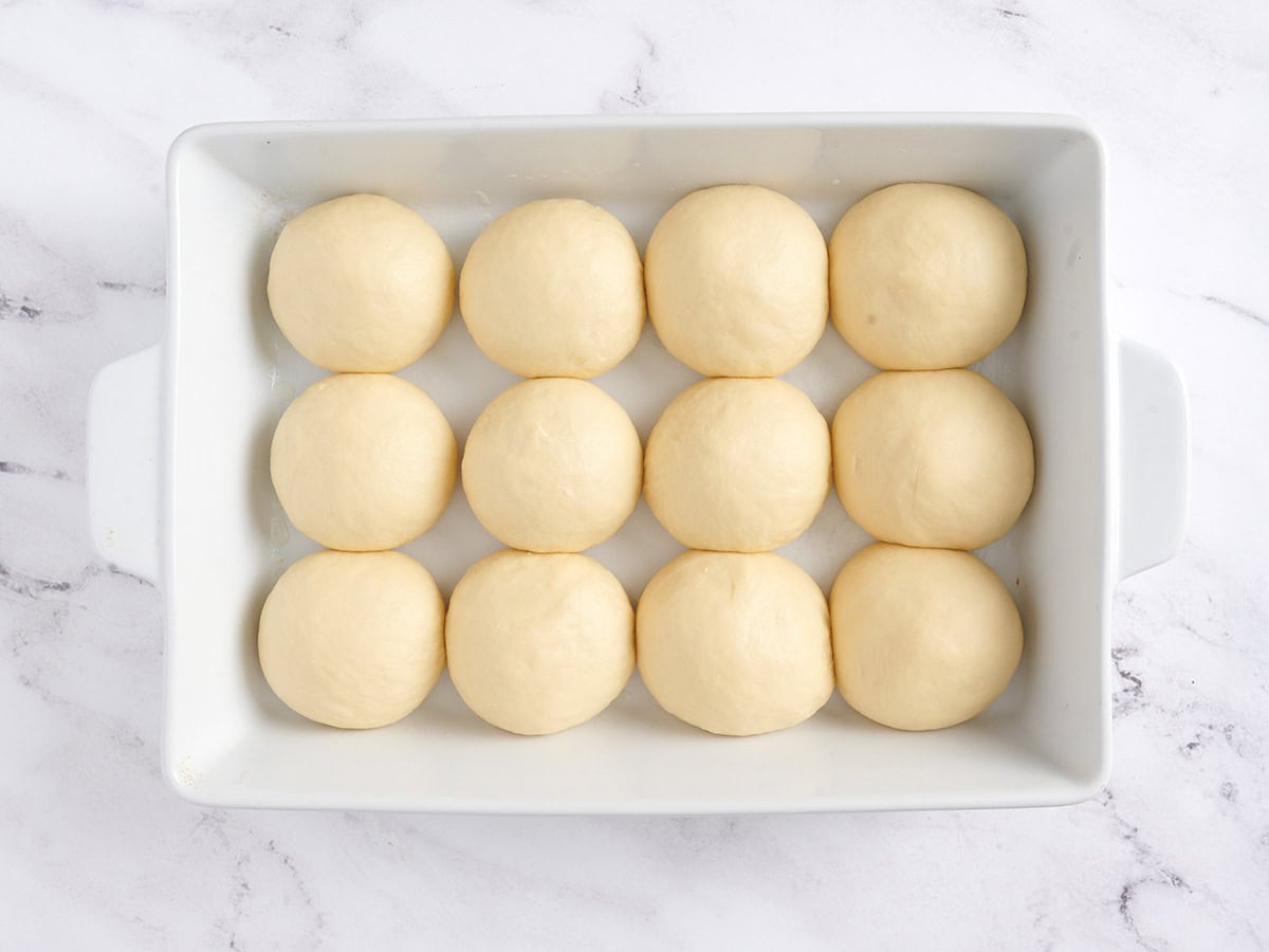 Proofed rolls in a white baking dish.