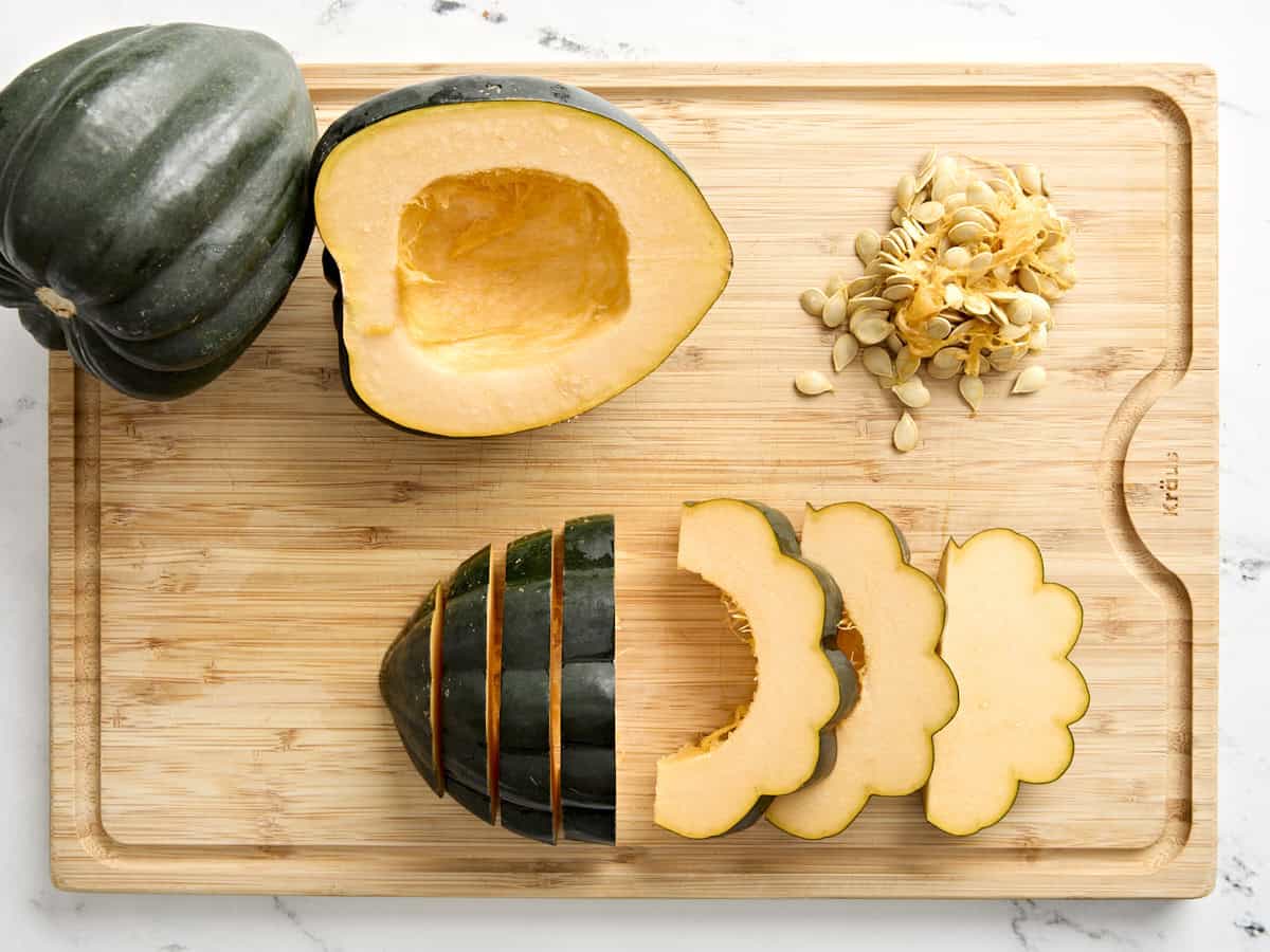 Half a deseeded acorn squash on a chopping board with the other half cut into slices.