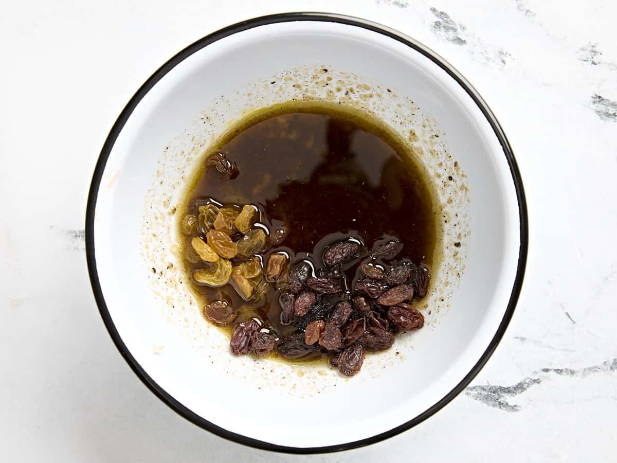 Oil, seasonings, and raisins added to a mixing bowl.