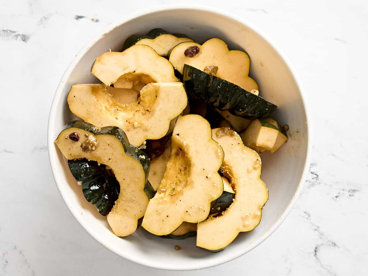 Acorn squash slices coated in oil, seasonings, and raisins in a mixing bowl.