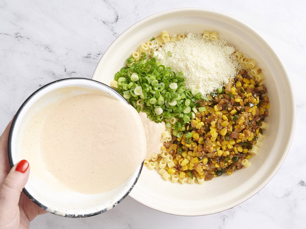 Cooked pasta, corn and vegetable mixture, green onions, queso fresco, and dressing in a bowl.