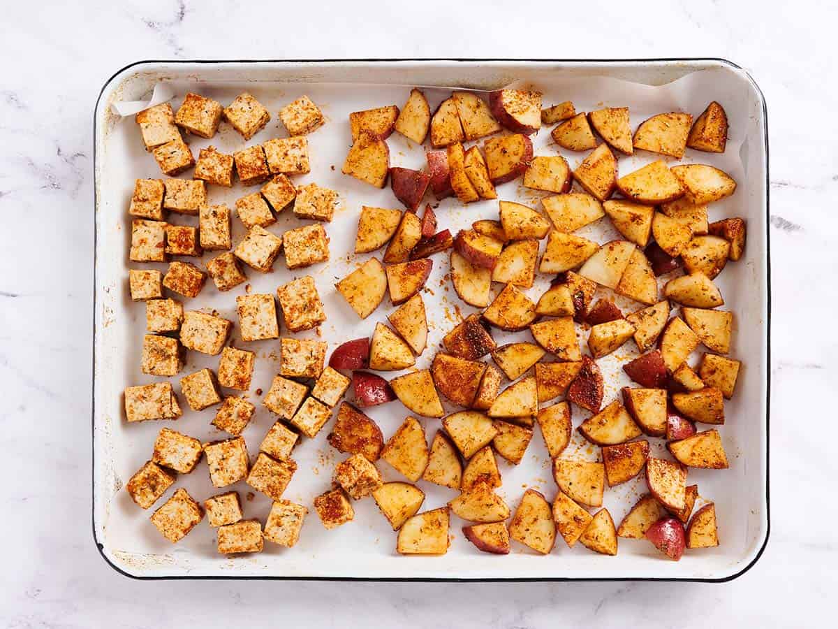 Seasoned tofu and potatoes on a parchment-lined sheet pan. 