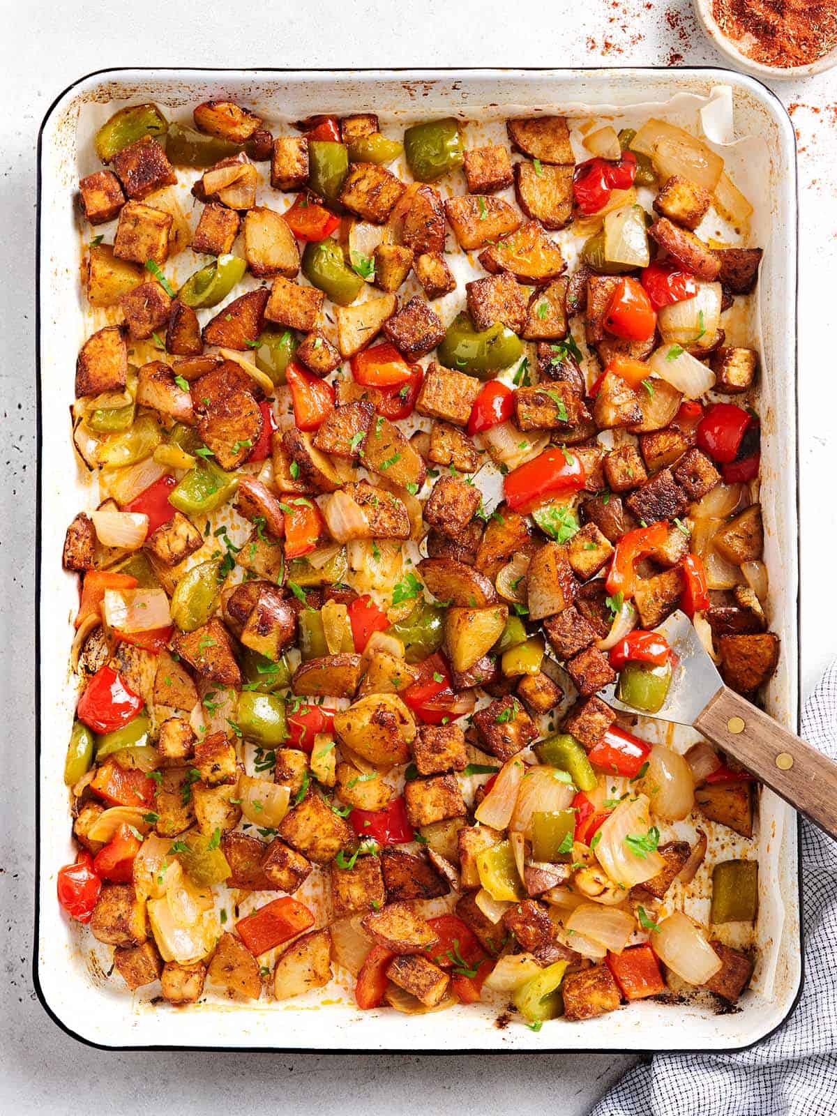 Sheet pan with Cajun tofu and vegetables and a spatula. 