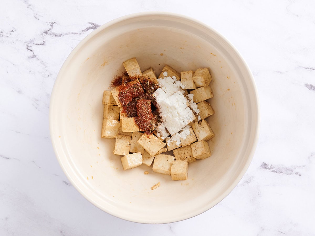 Cubed tofu with cornstarch and Cajun seasoning in a white bowl. 