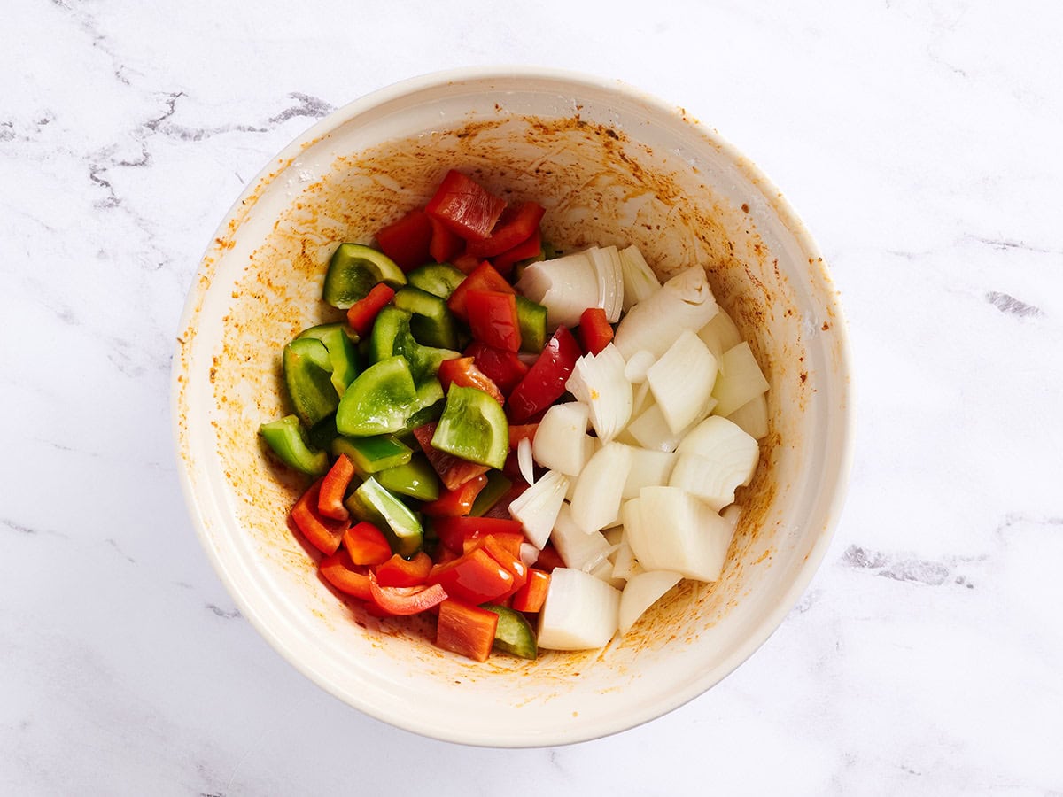 Bell peppers and onion in a white bowl with the Cajun seasoning. 