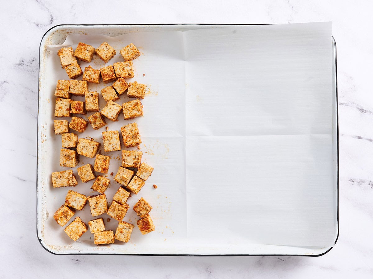 Seasoned tofu cubes on a parchment lined sheet pan. 