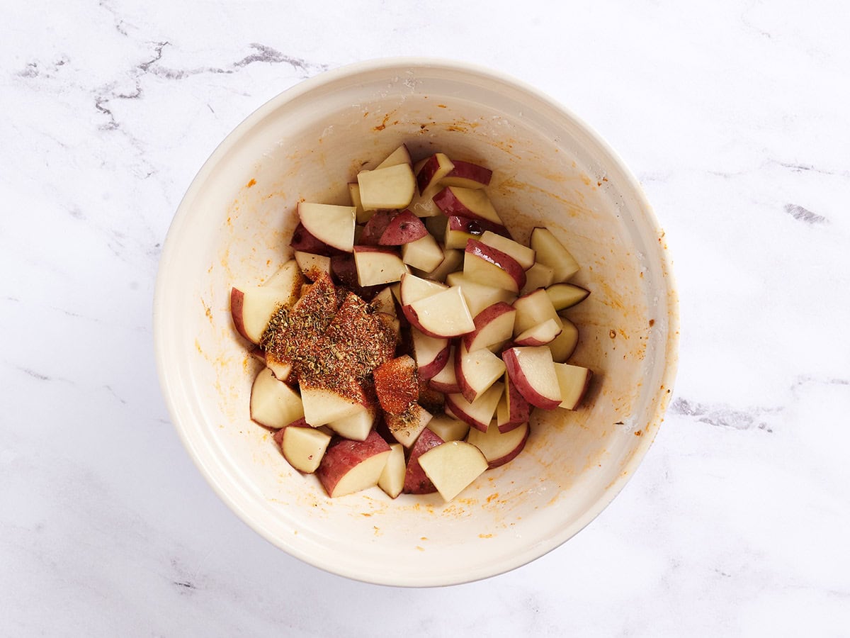 Cubed potatoes with Cajun seasoning in a white bowl. 