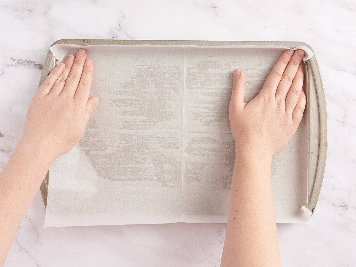 hands lining a baking sheet with parchment paper