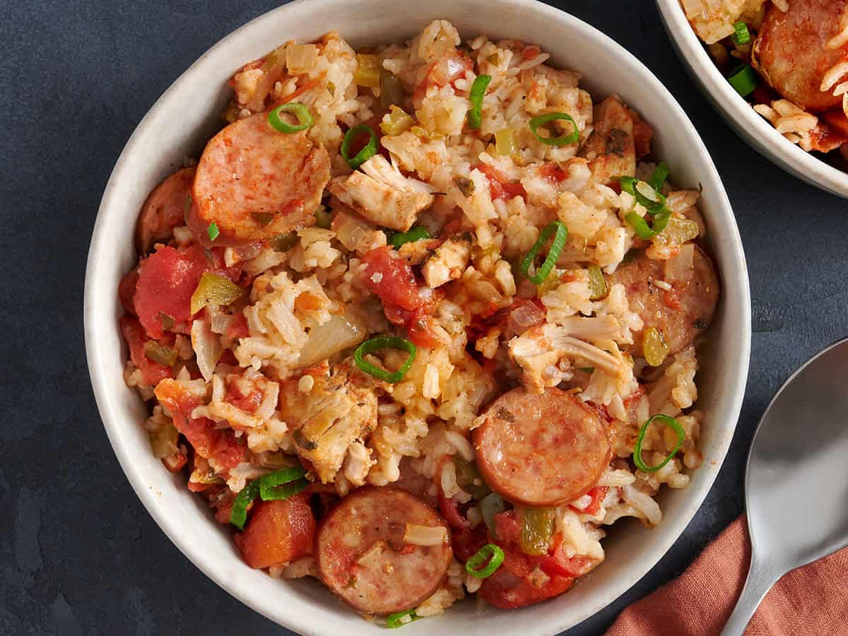 Bowl of slow cooker jambalaya garnished with green onions in a white bowl with a spoon.