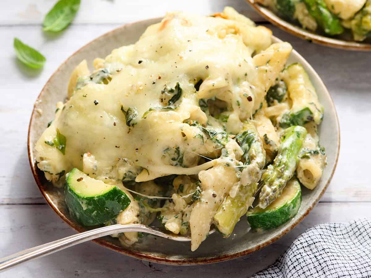 Side view of a plate of baked pasta with spring vegetable and a fork.