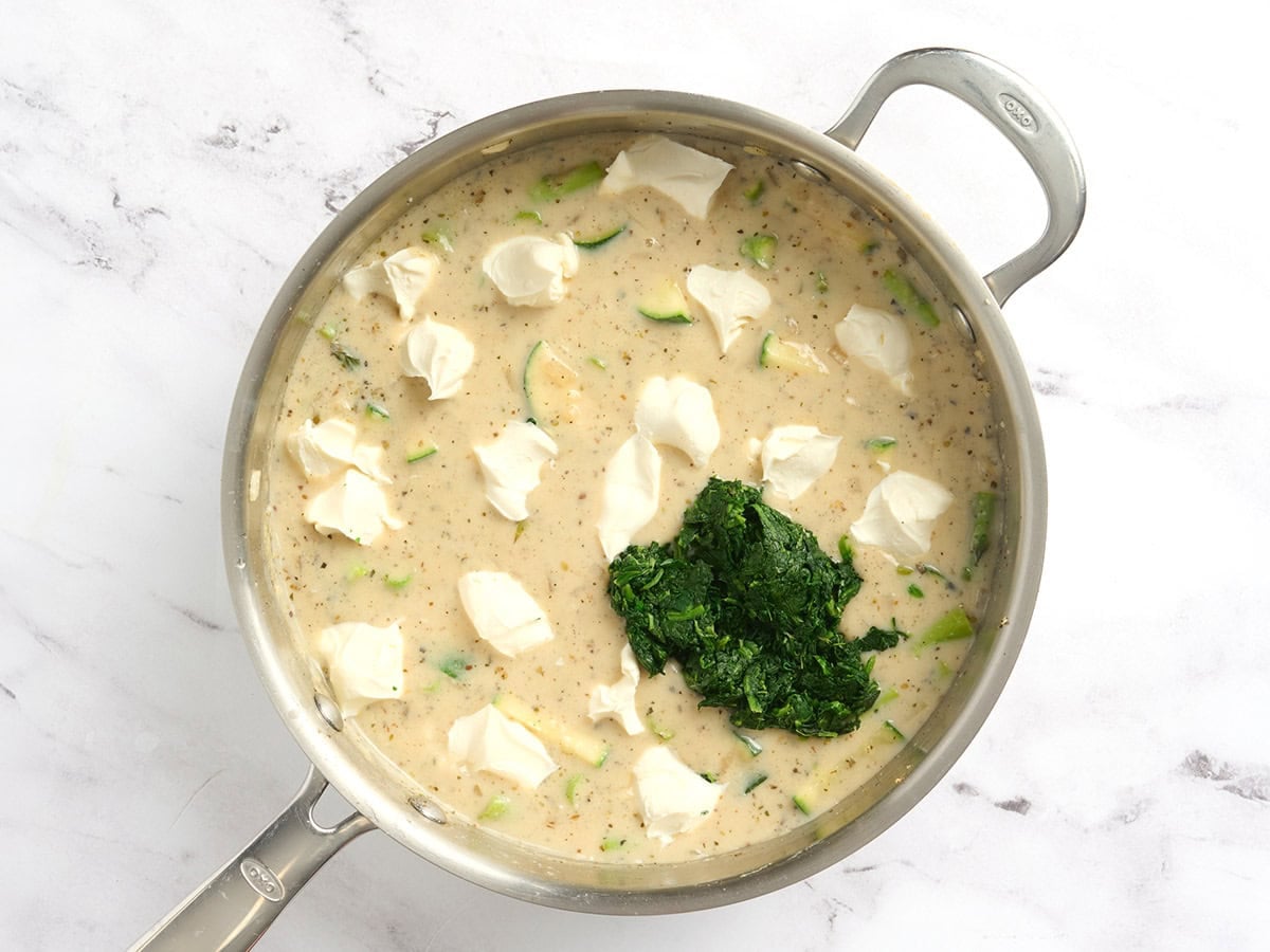 Cubes of cream cheese and thawed spinach added to a skillet of creamy sauce and veggies.