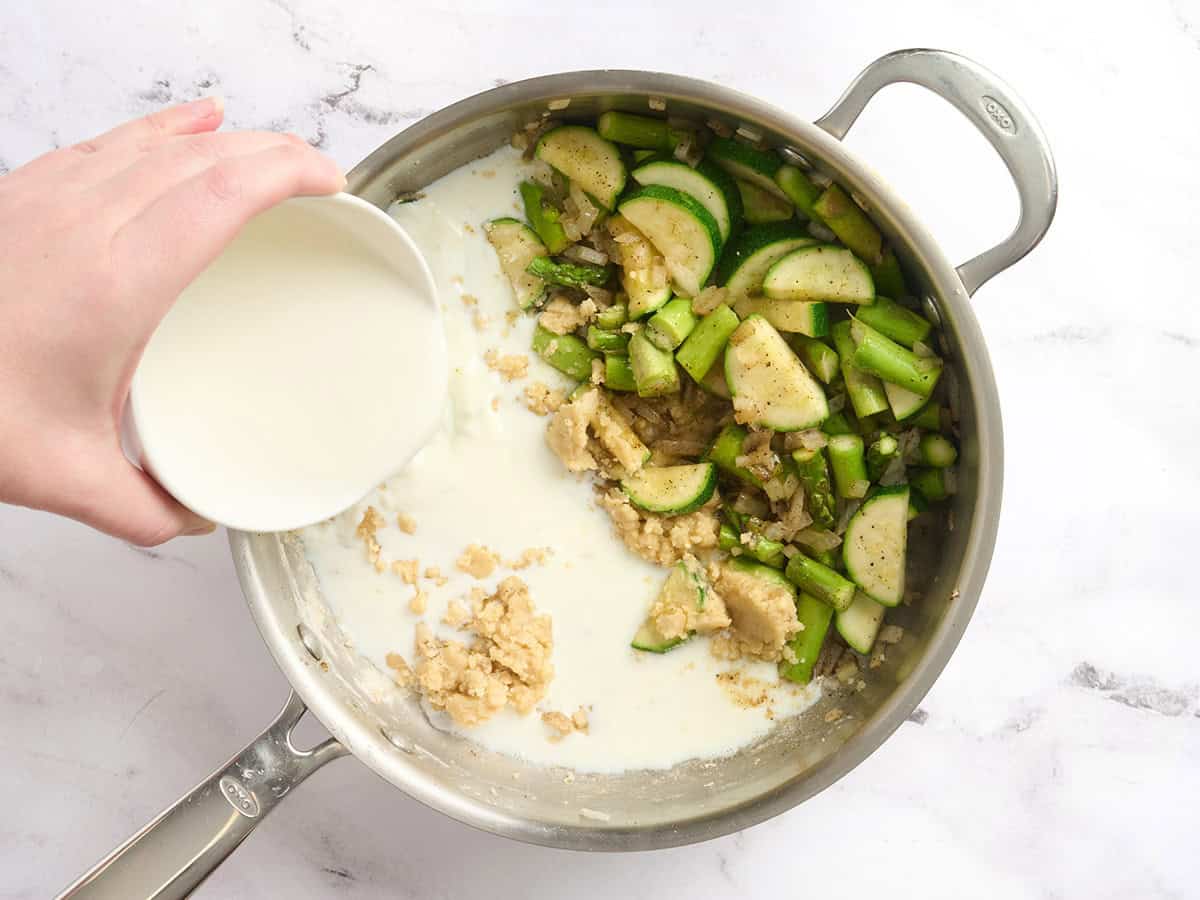 Milk added to a skillet of sauteed veggies.