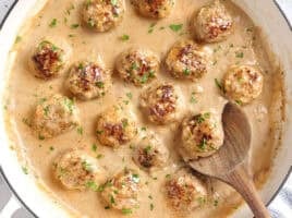 Overhead view of swedish meatballs in a skillet with a wooden spoon.