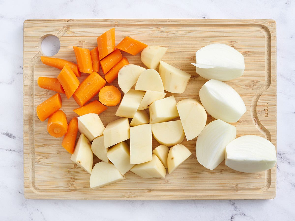 Sliced carrots, potatoes and onions on a wooden cutting board.