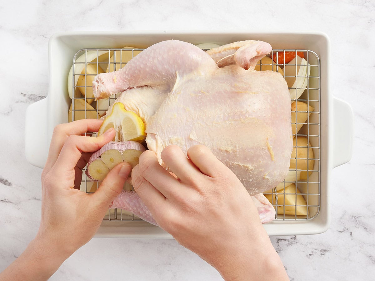 A whole chicken being stuffed with garlic and lemon.
