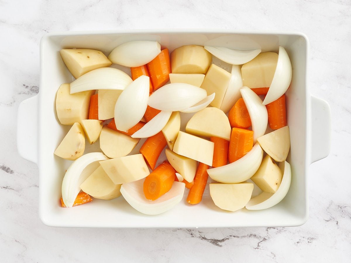 Potatoes, onions and carrots in a casserole dish.