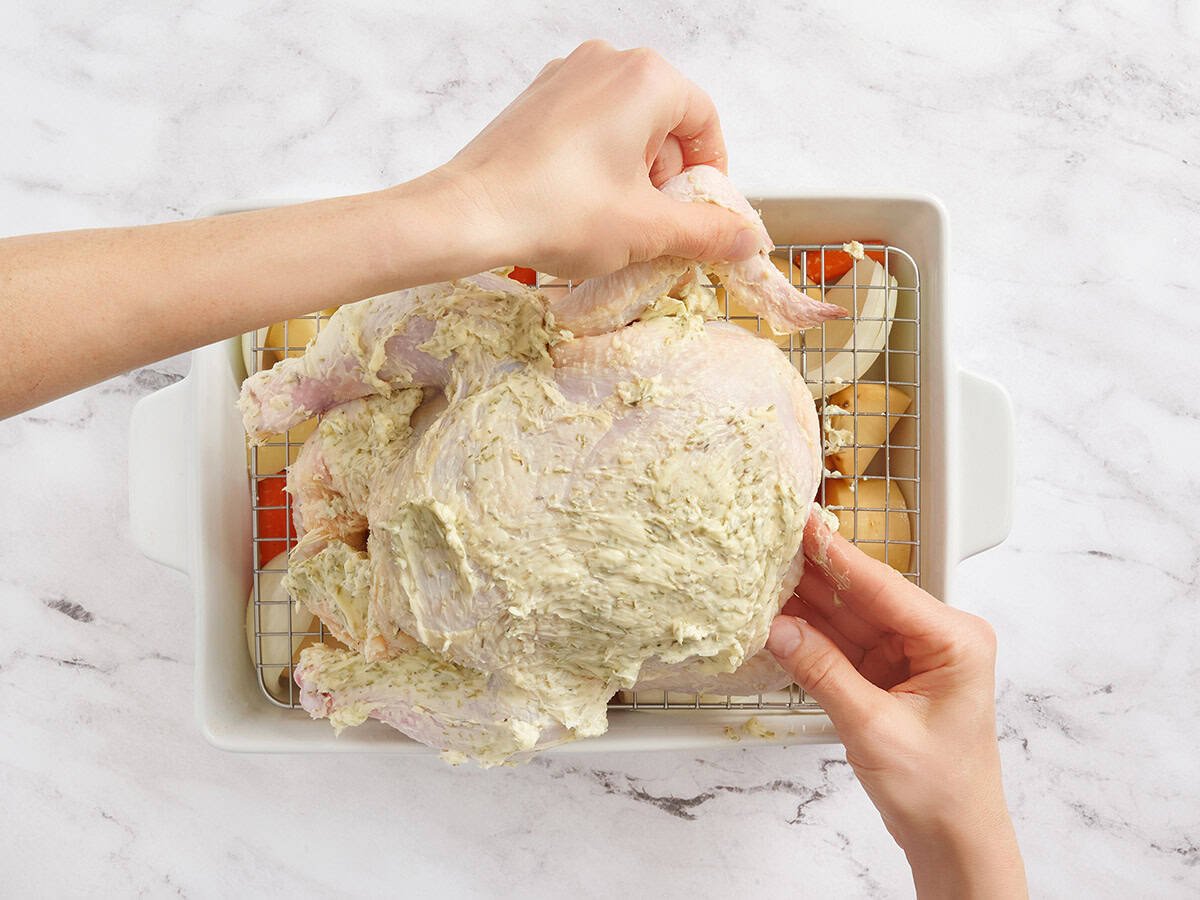 Hands tucking chicken wings under a whole chicken.