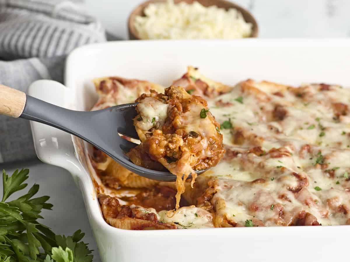 Side view of stuffed shells with meat with one shell being lifted out of a casserole dish.