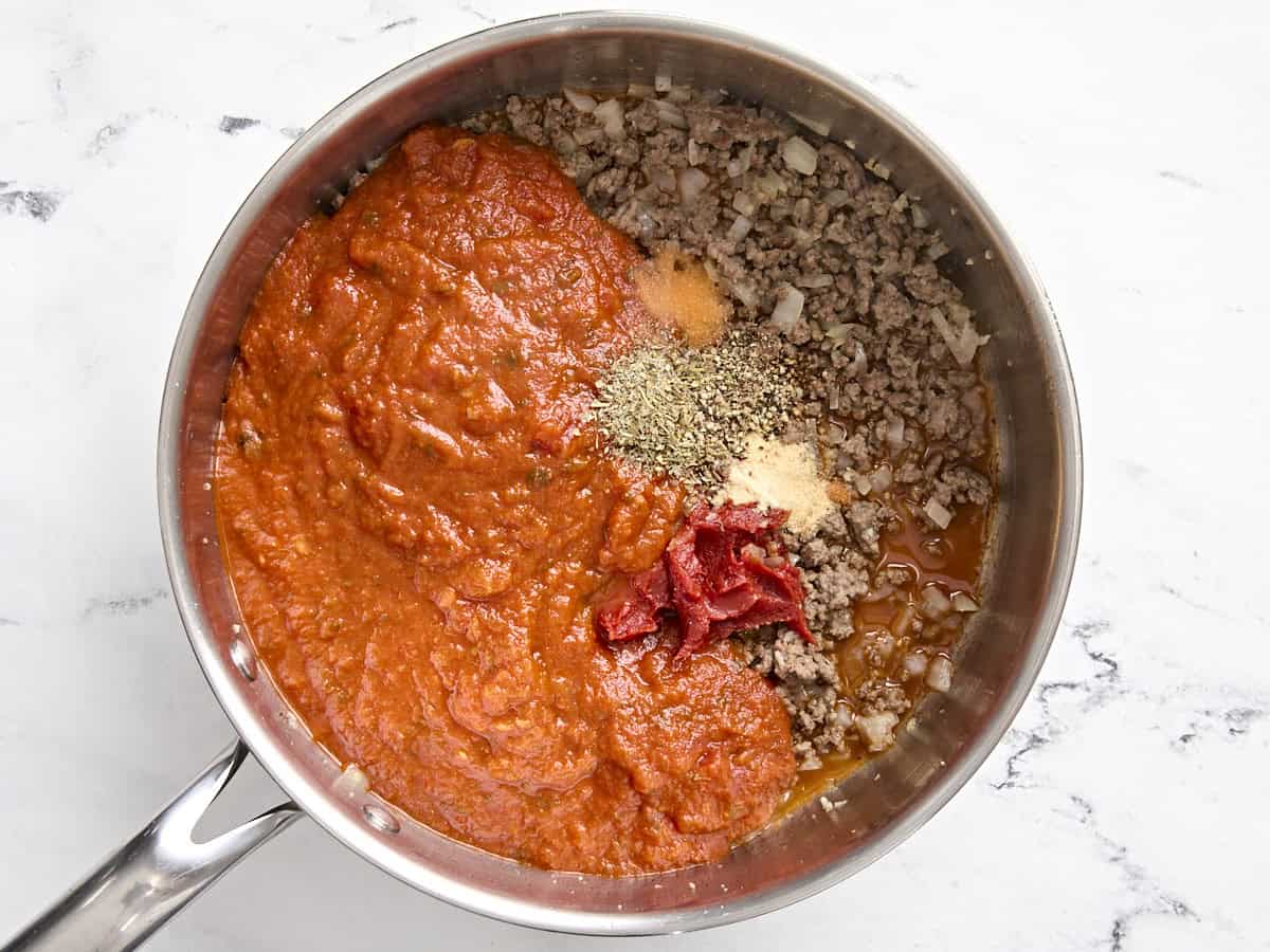 Marinara sauce, tomato paste, and spices added to beef in a skillet.