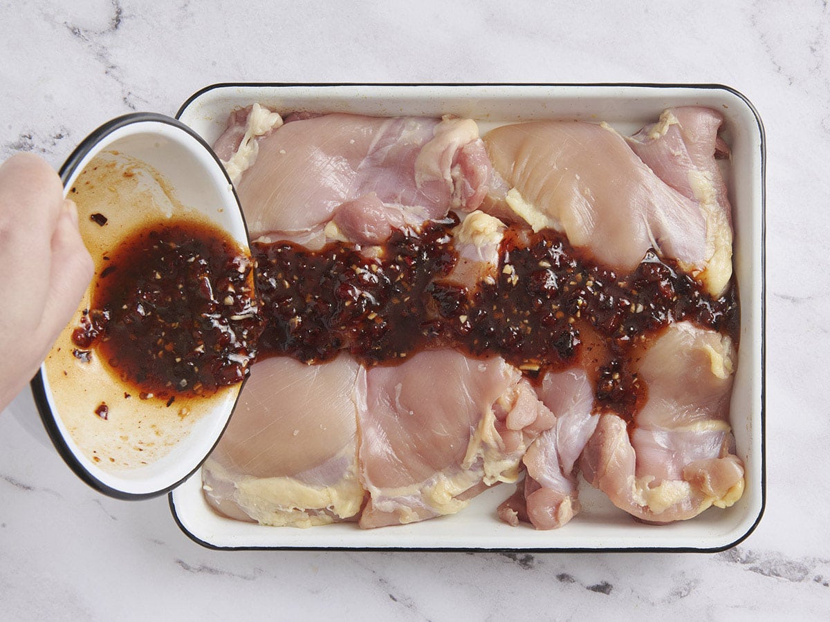 A chipotle honey marinade being poured over boneless and skinless chicken thighs.