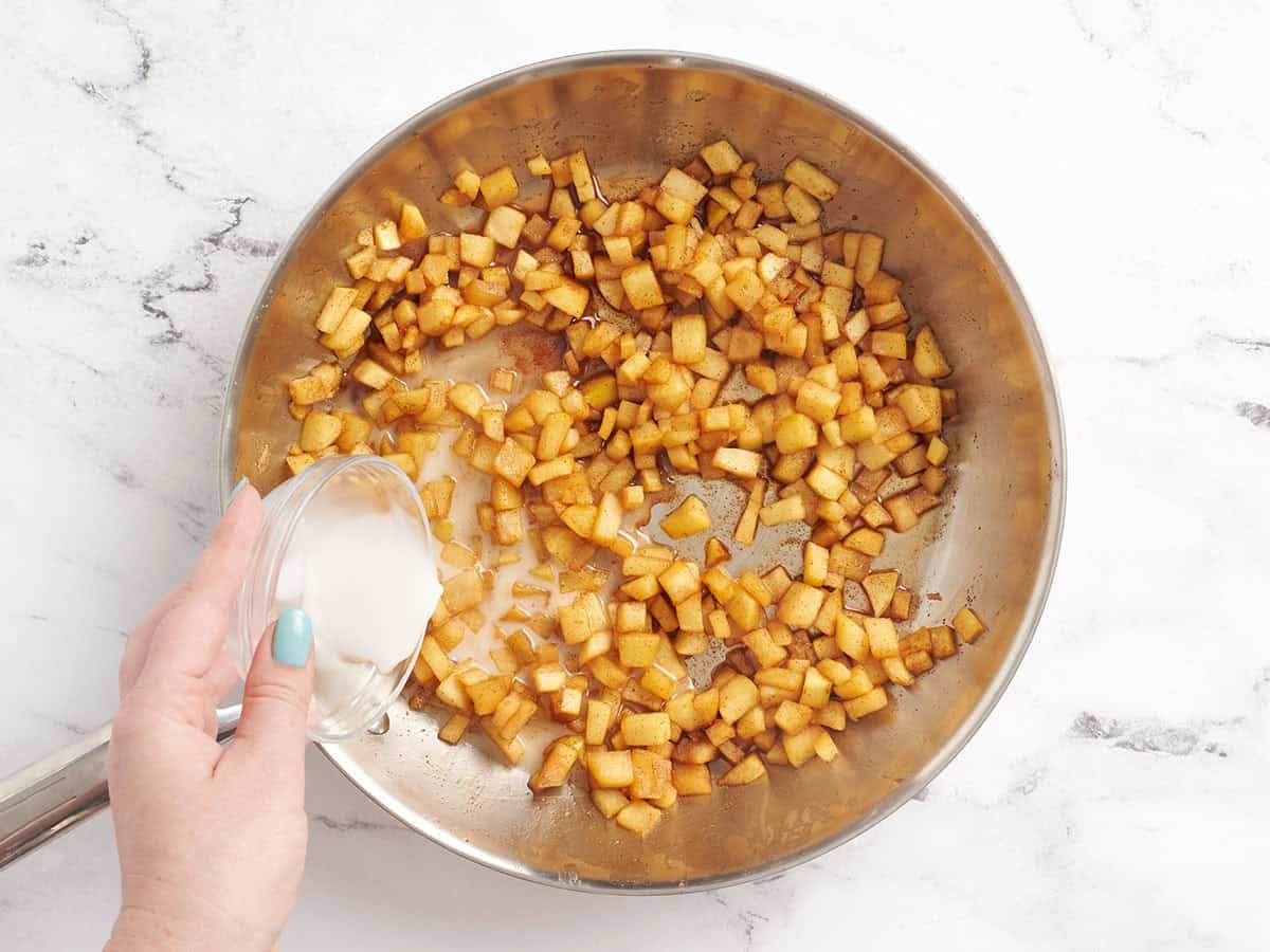 A cornstarch slurry being poured into a skillet with softened diced apple.