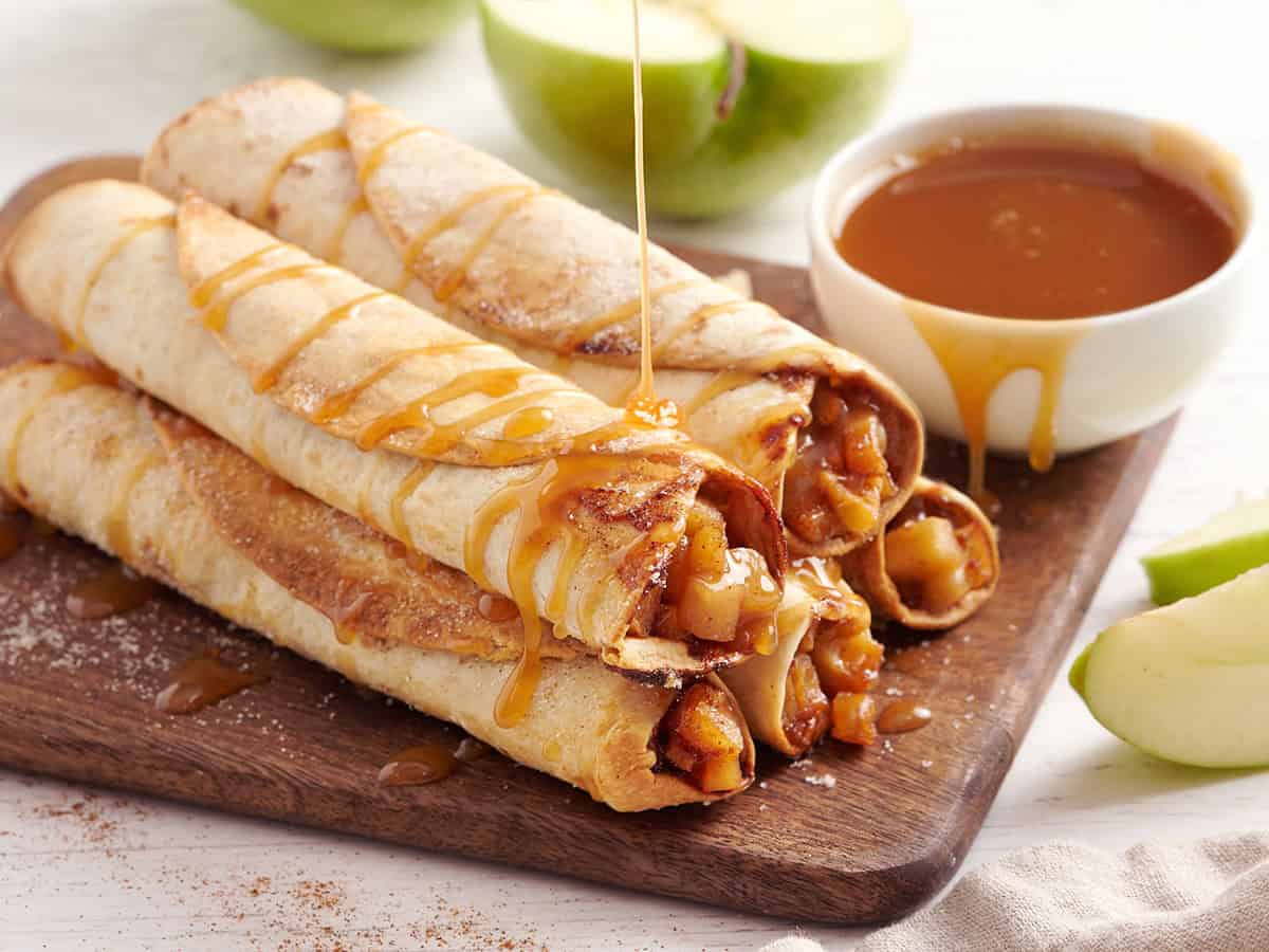 A stack of homemade apple flautas being drizzled in caramel sauce.