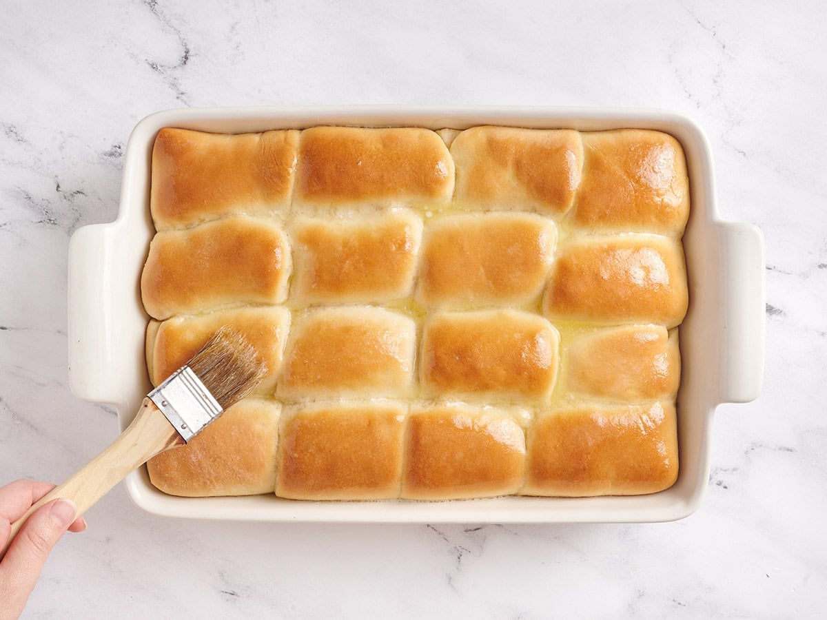 Brushing the tops of the baked rolls with butter.