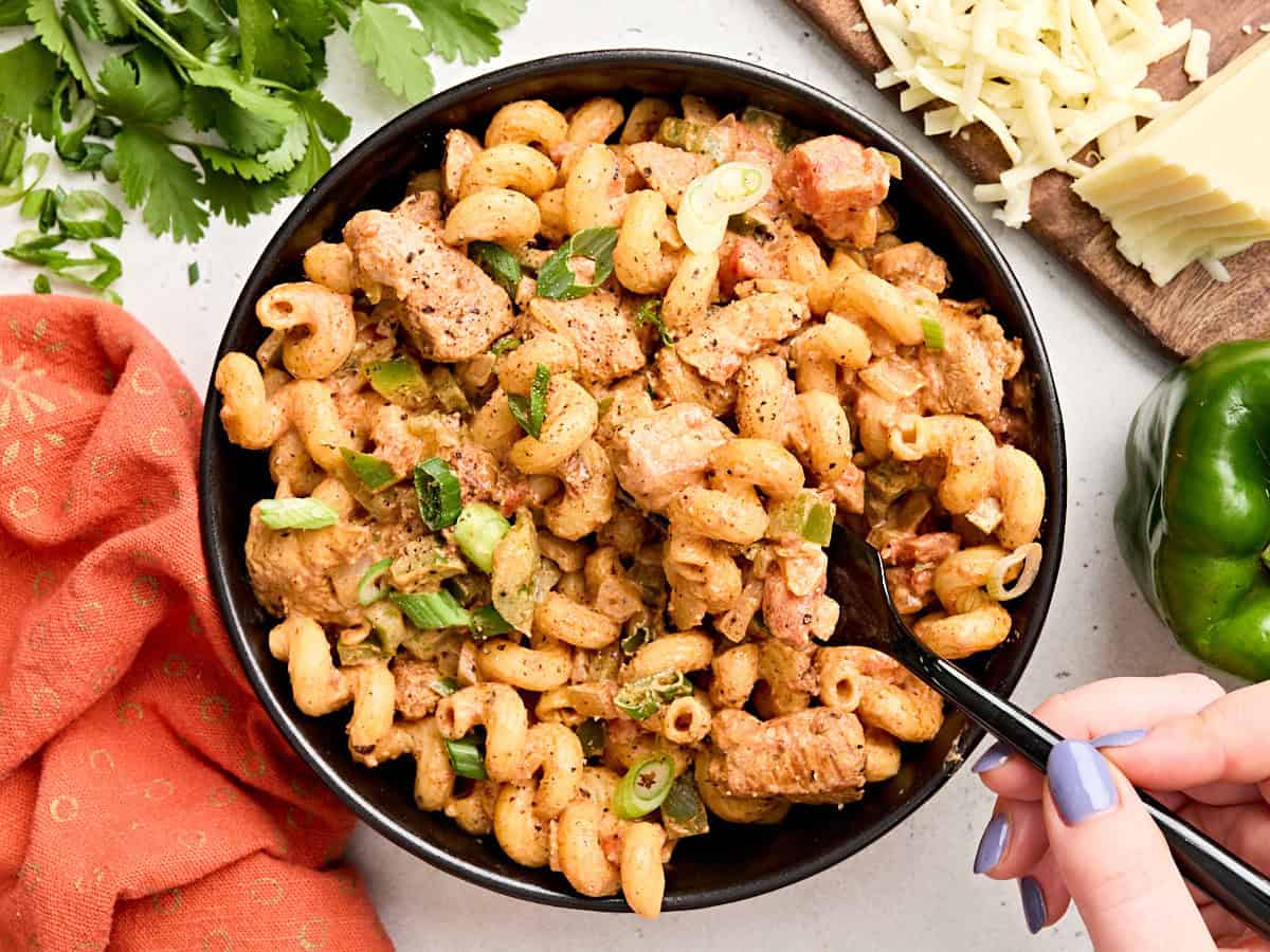 Overhead view of a bowl of creamy chicken fajita pasta, with a hand sticking a fork in.