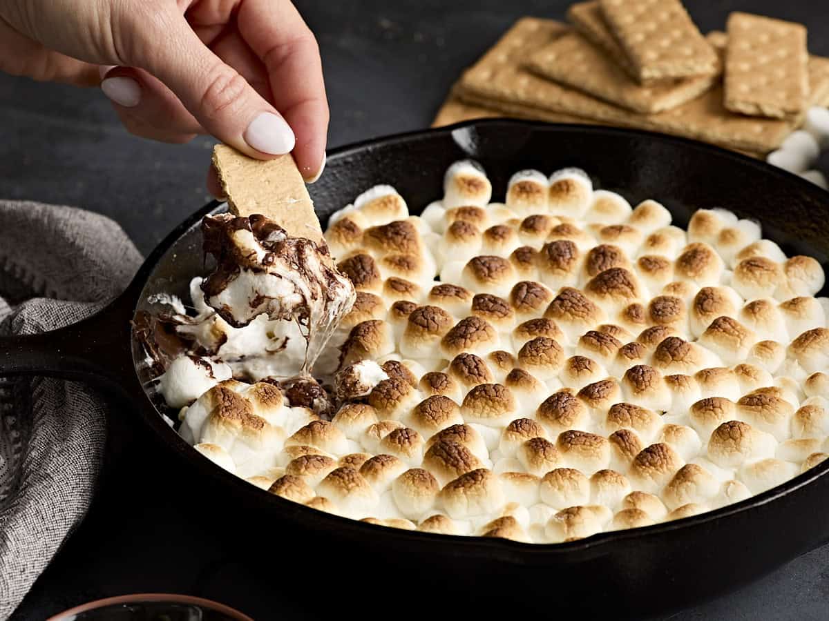 A hand dipping a graham cracker into s'mores dip