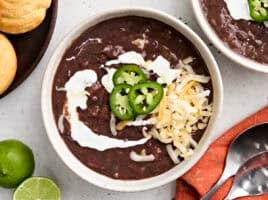 Overhead view of a bowl of black bean soup, topped with jalapeno slices, shredded cheese, and sour cream.