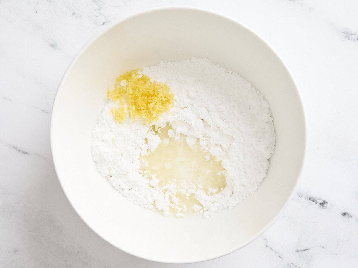 Lemon juice and lemon zest added to powdered sugar in a mixing bowl to make a simple lemon glaze.