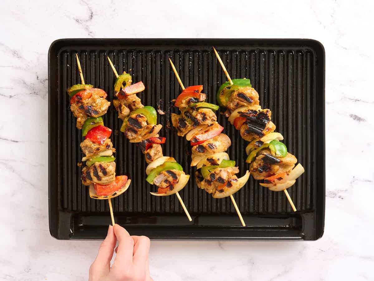A hand flipping a chicken and vegetable kabob over on a grill.