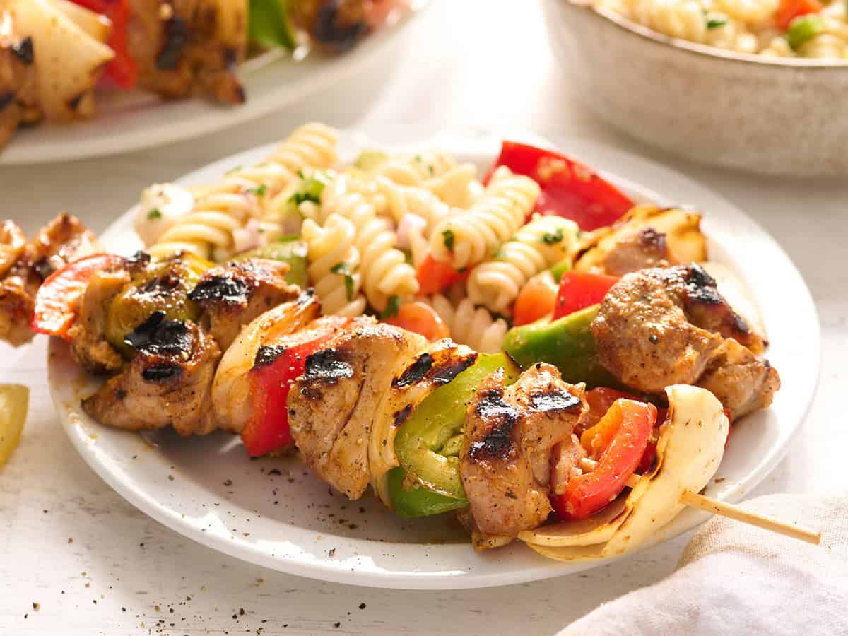 Side view of a chicken kabob on a plate with pasta salad.