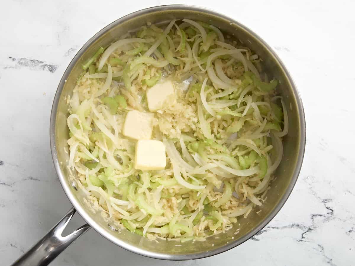 Butter and garlic added to a skillet with celery, onion, and parsnip