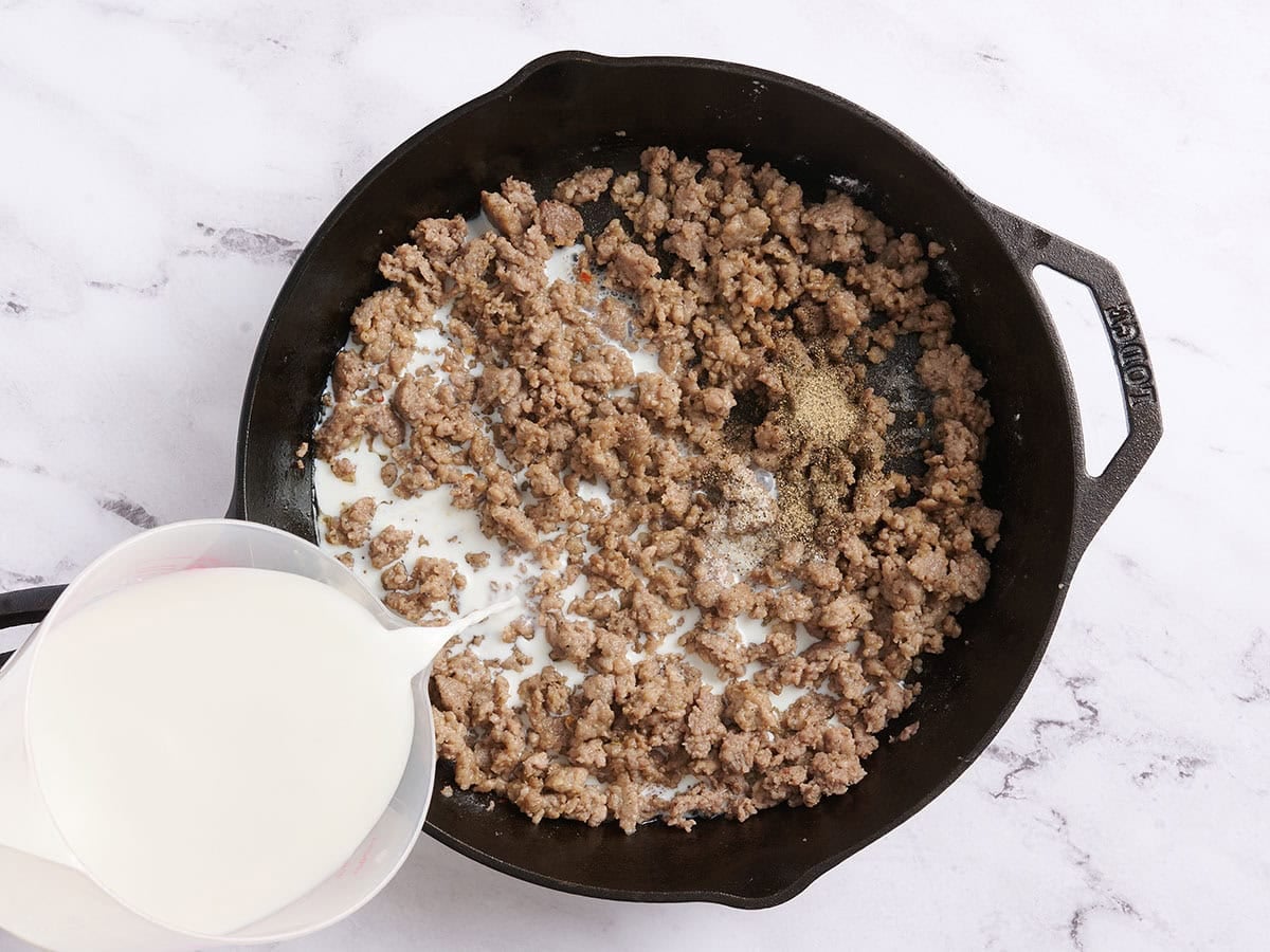 Milk being poured into browned sausage meat in a skillet.